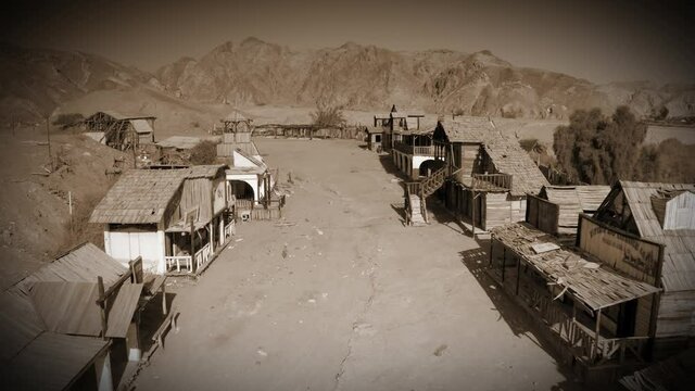 Wild west Town colored in old style Aerial view
Drone over Western town with desert mountains Old film look vignette and Sepia color 
