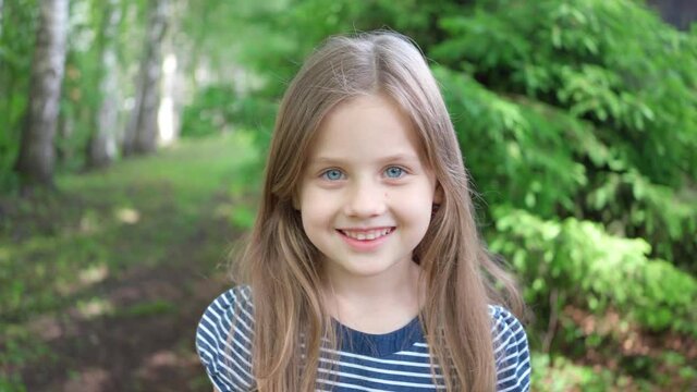 a little cute girl with blonde hair smiles at the camera. Close-up shooting. Vacation in the forest in summer, Beautiful girl with toothy smile, Dentistry, school holidays, vacation. Banner