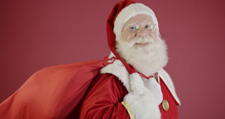 Real Santa Claus with a red background, wearing glasses, gloves and a hat looking side.