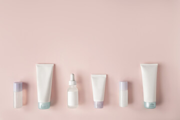 Beautiful spa composition of natural cosmetics mockup bottles of cream, serum and essence lined up on pink background. Top view. Flat lay style. Copy space.