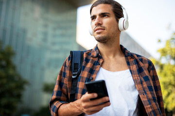 Young smiling man with headphones outdoors. Handsome man listening the music