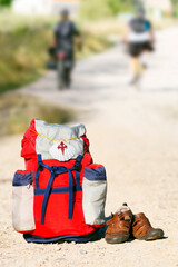 Way of St James , Camino de Santiago ,scallop shell on backpack  on dirt road with old sandals and...