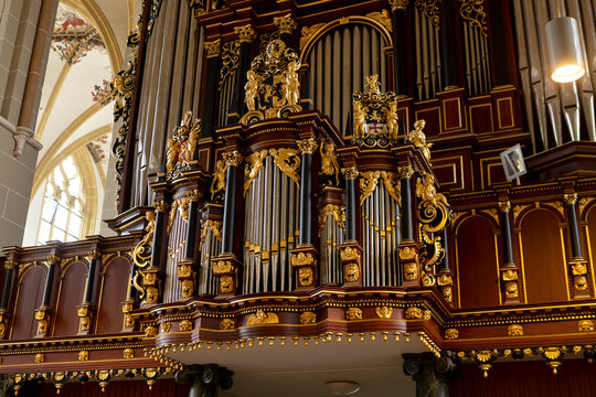 Richly decorated church organ with golden ornaments on the metal pipe structure. Religious music instrument in cathedral.