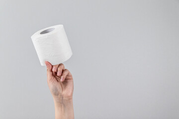 Female hand holds soft roll of toilet paper on a gray background with copy space. Minimal composition for advertising, article or banner