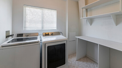 Pano Interior of a laundry room with wall mounted empty wooden shelves and desk