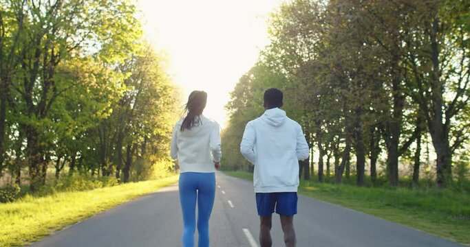 Back view of multi-ethnic sportsmen man and woman athletes running on street outside the city on sunset, family workout, sport and recreation African American male and Caucasian female jogging in park