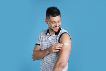 Vaccinated man with medical plaster on his arm against light blue background - obrazy, fototapety, plakaty