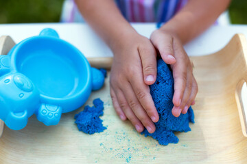 Hands of little girl playing with kinetic sand close-up. Leisure activity outdoors in summer day.