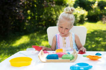 Little cute girl with blonde hair playing with kinetic sand outdoors in the backyard in summer day