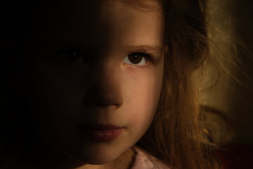 Little girl in dark side with shadow on face with blissful eyes  looking  dreaming or praying.  Soft focus. Indoor portrait with natural light coming from a window