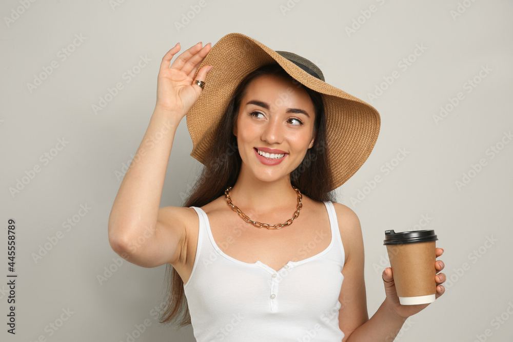 Sticker Beautiful young woman with straw hat and cup of coffee on light grey background. Stylish headdress