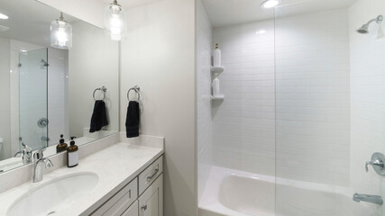 Pano Small modern plain white bathroom with an alcove bathtub with glass wall partition and white...
