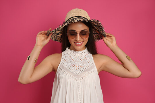 Beautiful young woman with straw hat and sunglasses on crimson background. Stylish headdress