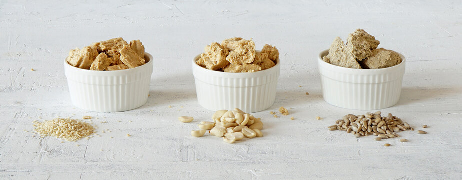 three bouls with halva of sesame seeds, peanuts and sunflower seeds  and the  seeds lie nearly on white background