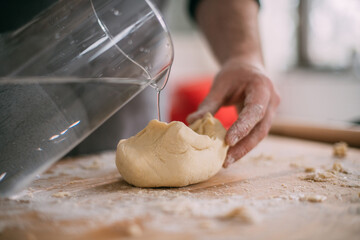 A male chef prepares noodle dough at home in the kitchen. Close up of hands with flour and dough