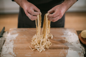 A male chef prepares noodles at home in the kitchen.