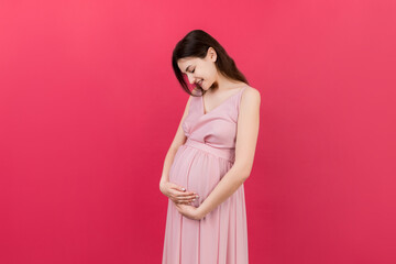 Happy pregnant woman touching her abdomen at Colored background. Future mother. Expecting of a baby. Copy space