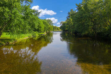 Fototapeta na wymiar Beautiful clear river gentle blue skies and delightfully green trees. The Milwaukee River runs through Saukville WI