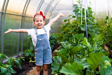 a little happy blonde girl in a greenhouse with her hands up rejoices, plant care, gardening concept for children