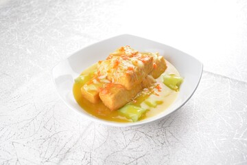 Deep fried bean curd tofu with luffa melon in yellow chicken stock sauce and crab meat on white background Asia halal menu