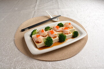 steamed bean curd tofu with minced prawn seafood on top and broccoli vegetables in dark soy sauce on white background Asia appetiser halal menu