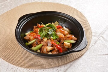 Stir fried spicy mala chicken meat with vegetables in black hot clay pot on white background Asia halal menu