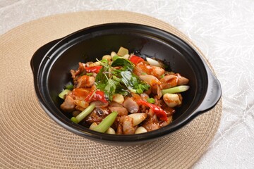 Stir fried spicy mala chicken meat with vegetables in black hot clay pot on white background Asia halal menu