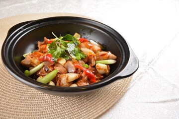 Stir fried spicy mala chicken meat with vegetables in black hot clay pot on white background Asia halal menu