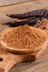 Dry carob pods and carob powder over wooden background. Organic healthy ingredient for vegan vegetarian food and drinks, close up