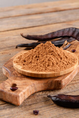 Dry carob pods and carob powder over wooden background. Organic healthy ingredient for vegan vegetarian food and drinks, close up