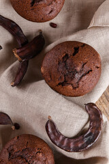 Chocolate carob cupcakes cooking with carob powder and dried carob pods on a wooden background. Organic healthy sweet food for vegan vegetarian food and drinks, close up
