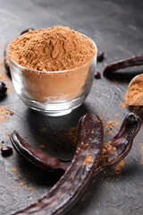 Dry carob pods and carob powder on a dark background. Organic healthy ingredient for vegan vegetarian food and drinks, close up
