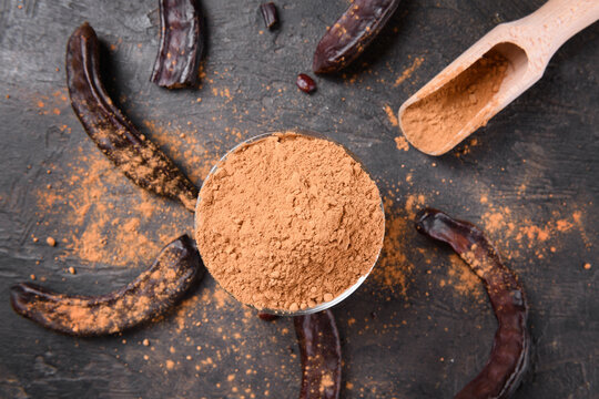 Dry carob pods and carob powder over dark background. Organic healthy ingredient for vegan vegetarian food and drinks, view from above
