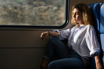 Girl passenger traveling by train sits on the seat and looks out the window