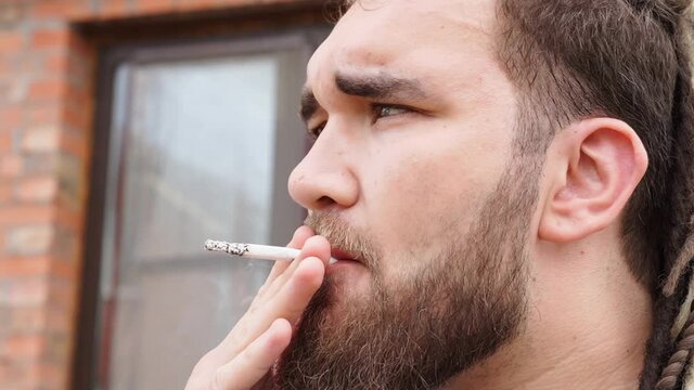 close-up. a man with a beard and dreadlocks smokes cigarettes and releases smoke