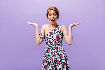 Happy Lady in floral dress shrugs on purple background. Joyful pretty woman with beautiful makeup in trendy outfit posing into camera..