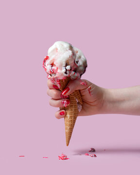 Fototapeta A female hand holds an ice cream cone on a pink background. The ice cream melted and ran down my fingers and hand. The hand squeezed and crushed the waffle glass.