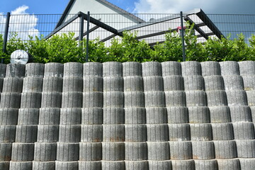 Stützmauer aus grauen runden Pflanzsteinen zur Hangsicherung und Abgrenzung eines Wohngrundstücks...