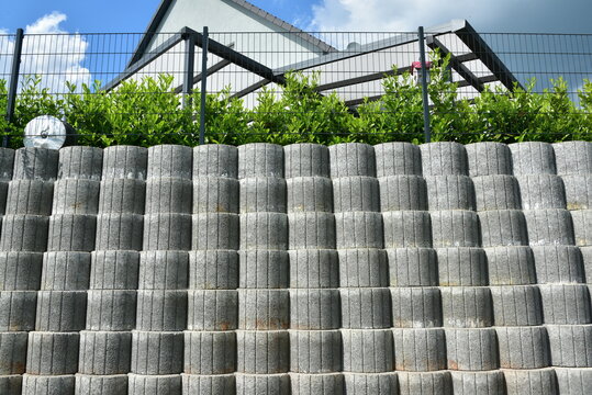 Stützmauer aus grauen runden Pflanzsteinen zur Hangsicherung und Abgrenzung eines Wohngrundstücks gegen die tiefer liegende Straße