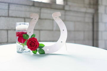 Closeup of table decorations with glass, red rose, and a horseshoe stand
