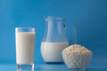 White milk in a jug and glass and cottage cheese on a blue background. Dairy product concept