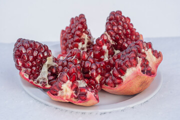 Open pomegranate fruit with red seeds on a white snow in winter, close up