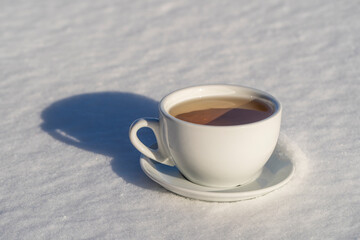 White cup of hot tea on a bed of snow and white background, close up