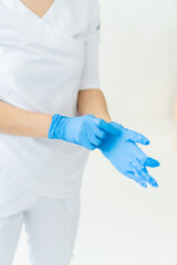 Medical concept. Nurse doctor surgeon dentist without face wear white costume puts on rubber disposable sterile blue gloves isolated on white soft blure background. Verical photo. Focus on hands,