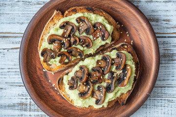 Tasty sandwich with green mashed avocado, fried mushrooms and sesame seeds in