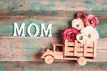 Wooden toy truck with peonies flowers in the back and word MOM on wooden turquoise boards. Space for text.