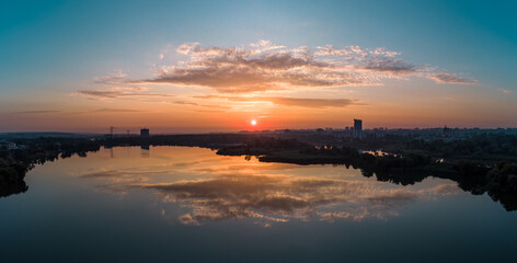 Scenic wide panorama aerial sunrise with clouds reflecting in mirror water surface on wide river. Early morning, dawn in Kharkiv Zhuravlivskyy Hidropark from sky. Drone photography