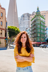 Fototapeta premium Beautiful young woman in a yellow shirt in a business center with a view of the Transamerica Tower in San Francisco