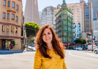 Fototapeta premium Beautiful young woman in a yellow shirt in a business center with a view of the Transamerica Tower in San Francisco