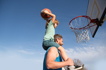 Father and son playing basketball. Happy father holding his little son on shoulders, helping him to...